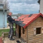 Männlicher Helfer der das Dach eines Spielhauses mit Dachpappen erneuert